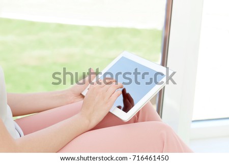 Young woman using tablet for searching information in internet on window sill