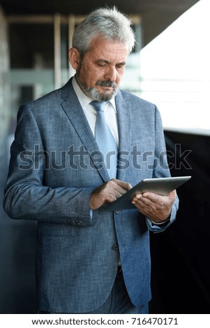 Portrait of a senior businessman with tablet computer outside of modern office building. Successful business man in urban background wearing suit and tie.