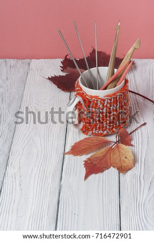 Autumn still life cup of coffee on wooden table. ?nitted sweater with autumn leaves, spokes, crochet and coffee mug. Autumn moody style background. Top view.