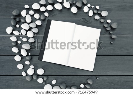 Black open book lying on a gray table with white and stones. Concept of a new exciting story. 3d rendering mock up
