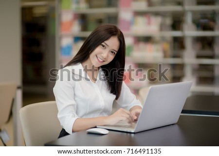 Portrait of a happy beautiful Asian student girl using laptop in a library
