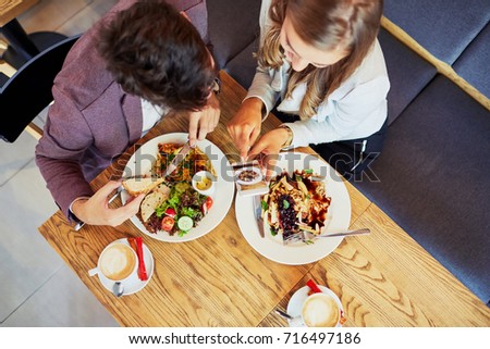 Cute young couple eating together and taking photos of their food in a restaurant