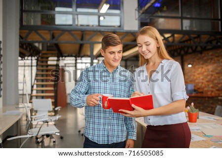 Man with a red cup, girl with a red notebook. Coworkers working together in modern coworking studio. Talking with colleague about new startup project. Horizontal.