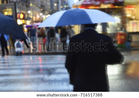 Rain in New York City. Man with blue and white umbrella crosses the street, blurred picture