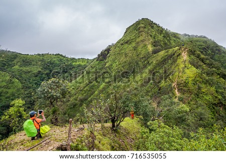 Hikers with backpacks stand on the mountain ridge taking a photo to the mountain peak.