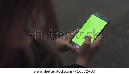 female teen girl using smartphone with green screen sitting outdoors