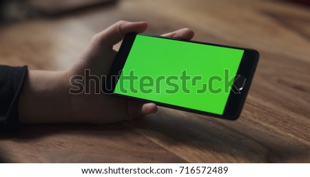 female teen girl hold smartphone with green screen over wood table