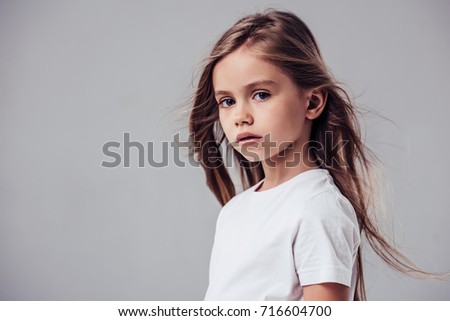 Little cute girl with flying hair isolated. Charming blonde is posing on white background and looking at camera.