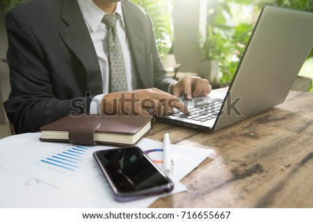 businessman using laptop and smart phone for work, analyze marketing strategy with statistic graph and notebook on wooden desk.stock trading analysis.