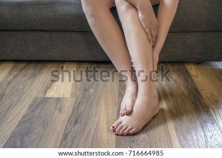 Young woman sitting on the couch suffering from severe pain in the leg. Woman suffering from leg pain.