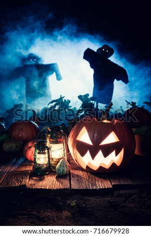 Scary Halloween pumpkin with blue mist and scarecrows