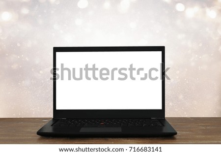 Image of open laptop with white screen on wooden table in front of abstract glitter background.