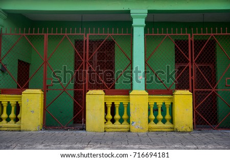 Green house with small yellow fence and metal gates.
