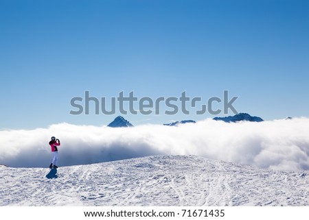 Female tourist skier taking picture of spectacular mountains, white clouds and clear blue sky view