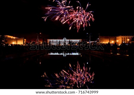 Beautiful festive fireworks, salute above buildings in the city and its reflections in the fountain on the background of the black sky