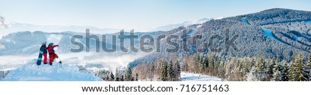 Extra wide panorama of the Carpathians mountains landscape, forests in a white haze, ski slopes, winter ski resort Bukovel. Two snowboarders enjoying, resting on top of the mountain on a sunny day Royalty-Free Stock Photo #716751463