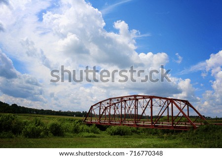 red bridge with green fields and big blue sky with white puffy clouds 
