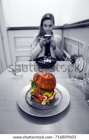 Young woman in a restaurant with a hamburger photographing a meal on a table