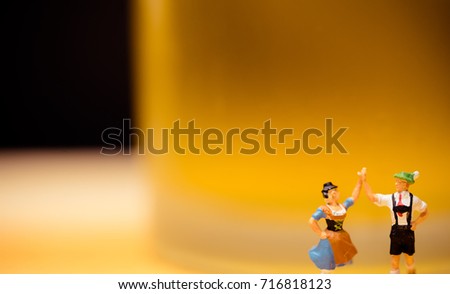 Miniature people.Bavarian man and girl in traditional Dirndl dresses are dancing having fun at the Oktoberfest in glass of beer.Oktoberfest Munich in Germany.People dressed in traditional costumes.