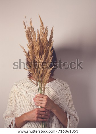 woman holding a bouquet of dry grass in front of her face with spikelets, no faces visible