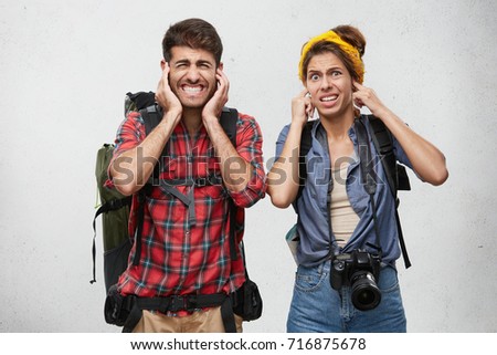 Stressful man and woman hear unpleasant irritated loud sound, plug ears, look disconent and tired. Young hitch hikers see car accident on street with great crash, try escape from awful noise
