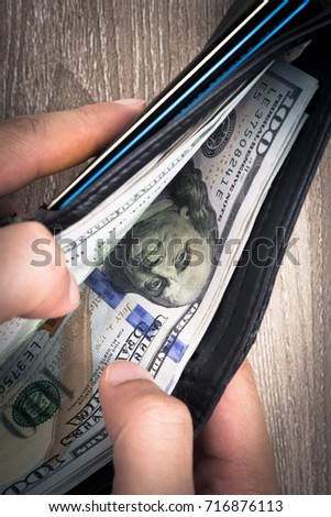 Men's hands holding and open black leather wallet with credit cards and stack of US dollar money.
