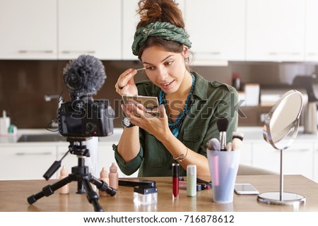 Attractive talented female blogger does make up, reviews beauty product for video blog, gives advice to girls and women, films process on camera. Fashionable woman has online translation at home Royalty-Free Stock Photo #716878612