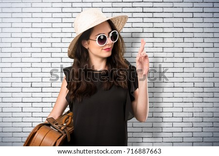 Beautiful young girl with  a suitcase with her fingers crossing on a brick wall
