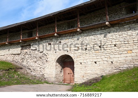 Long fortress wall with closed steel doors. The Trinity Cathedral. View from the inner area. The Pskov Krom or Kremlin. Russia