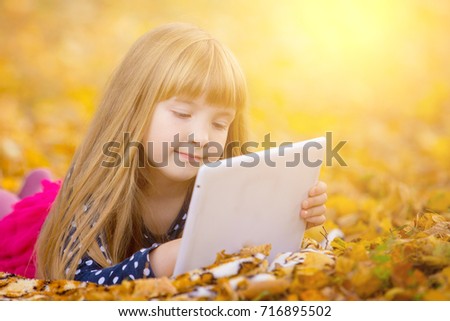 Little girl laying on grass and leaf and playing tablet pc