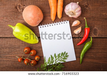 Fresh vegetables with a notepad lie on a wooden background. Bulgarian pepper, chili, potatoes, garlic, carrots and cherry tomato on a wooden table. Space for text.