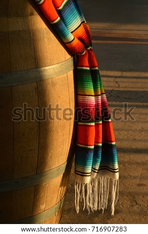 decorative Mexican woven blanket brilliant colorful stripes and white hanging fringe hanging over wooden barrel Royalty-Free Stock Photo #716907283