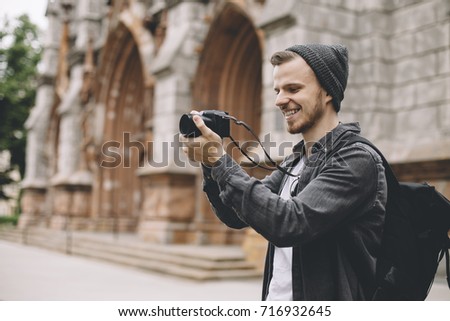 The photo of a tourist that likes to take pictures of city landscapes. He is standing near the old building and taking the pictures with passion and pleasure. Close up. Cut view