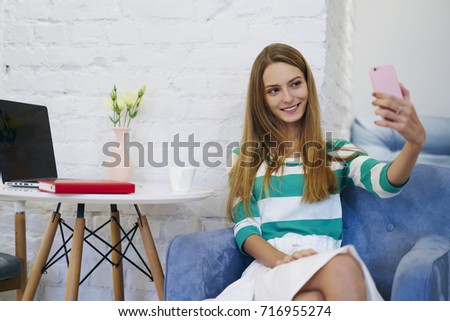 Cheerful young woman dressed in casual wear making selfies on smartphone camera having break while doing remote job in cafe,beautiful female blogger taking photo posing on modern interior coffee shop