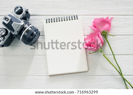 Blank notebook with pink rose and camera on table