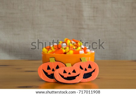 candy corn in an orange bowl with tiny jack-o-lanterns on a wooden table
