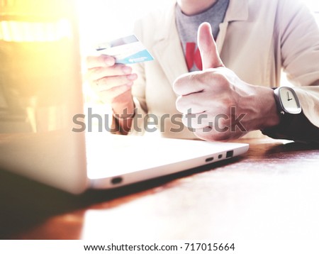 A man wear a white suit is thumbs up for an online Financial Transactions with credit card and white laptop. Online Financial Transactions concept. selective focus