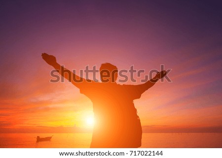 Silhouette of a man with hands raised in the beautiful sunrise.