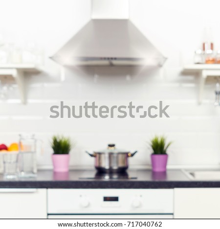 Blurred interior of a light kitchen in the apartment. Bright home interior decoration items, fruit, flowers in a pot, steel hood. Bright ready-made picture for your individual design  