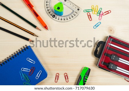 Top view of blue notebook, pen, pencils, protractor, colorful paper clips, set for drawing  and  pencil sharpener on wooden background. School stationery, office and student accessories.