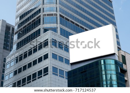 Blank advertising billboard on top of modern building in the city with blue sky background useful for products advertisement