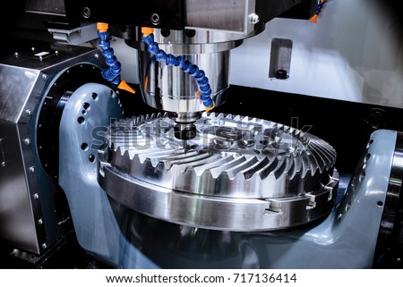 A modern CNC milling machine makes a large cogwheel. Accurate metal working. Shooting in real conditions, maybe some blurring and grain. Royalty-Free Stock Photo #717136414