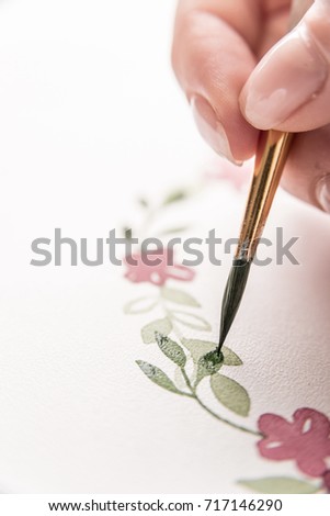 Close up of young artist drawing flowers pattern with watercolor paint and brush on paper at workplace