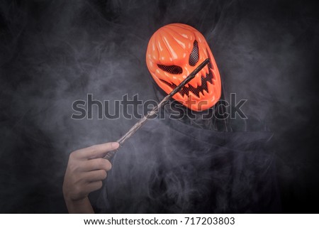 Mystery man with orange pumpkin evil mask holding magic wand in smoke scene, Halloween night costume concept