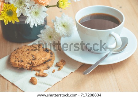 Cup of coffee and spoon on white plate, with almond chocolate ship cookies on wooden table background.