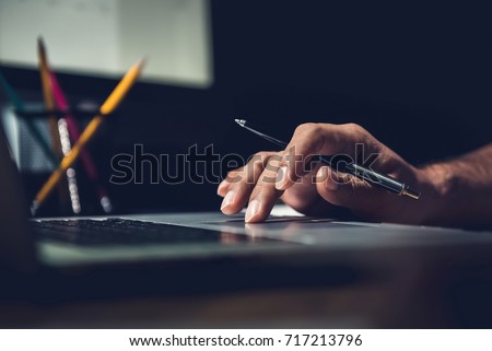 Hand of a man using laptop computer working overtime at his desk in the office late at night Royalty-Free Stock Photo #717213796