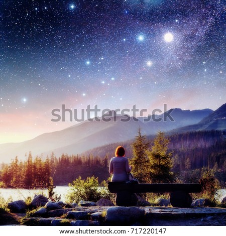 Lake Strbske pleso in High Tatras mountain, Slovakia, Europe. Fantastic starry sky and the milky way. The girl sits on a bench and looks into the fairy-tale sky. Courtesy of NASA.