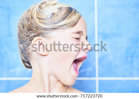 Child girl crying because she has foam in her eyes. Adorable child blond girl with shampoo foam on hair taking bath. Closeup portrait of smiling kid. Health care and hygiene concept.