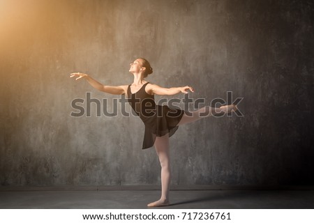 beautiful young blonde ballet dancer in a black dress, white pantyhose and bouillant pointes dancing Russian ballet in a dark dance studio