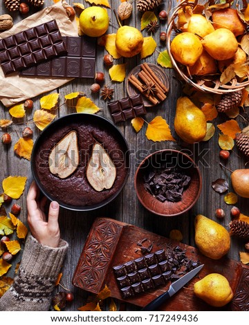 Chocolate Brownie with a pear in a baking dish is hold by a female hand in a sweater. Food gathering style. Autumn background. Ingredients for its preparation. Flat lay instagram food composition.